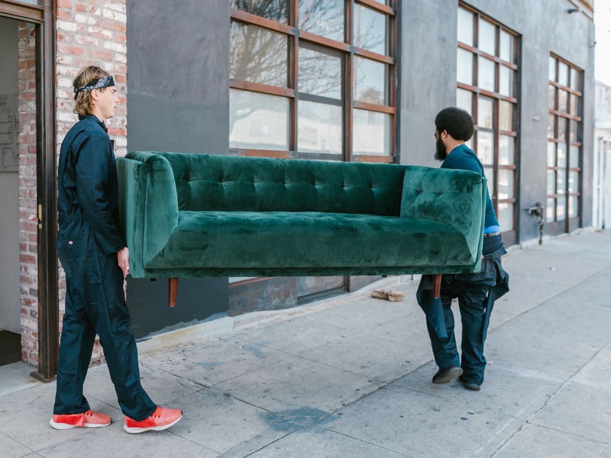Two professional movers carrying a wrapped sofa out through a doorway during a house move