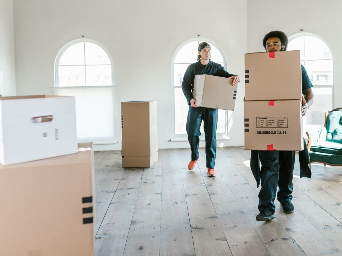Movers carrying labelled cardboard cartons into a bright empty apartment
